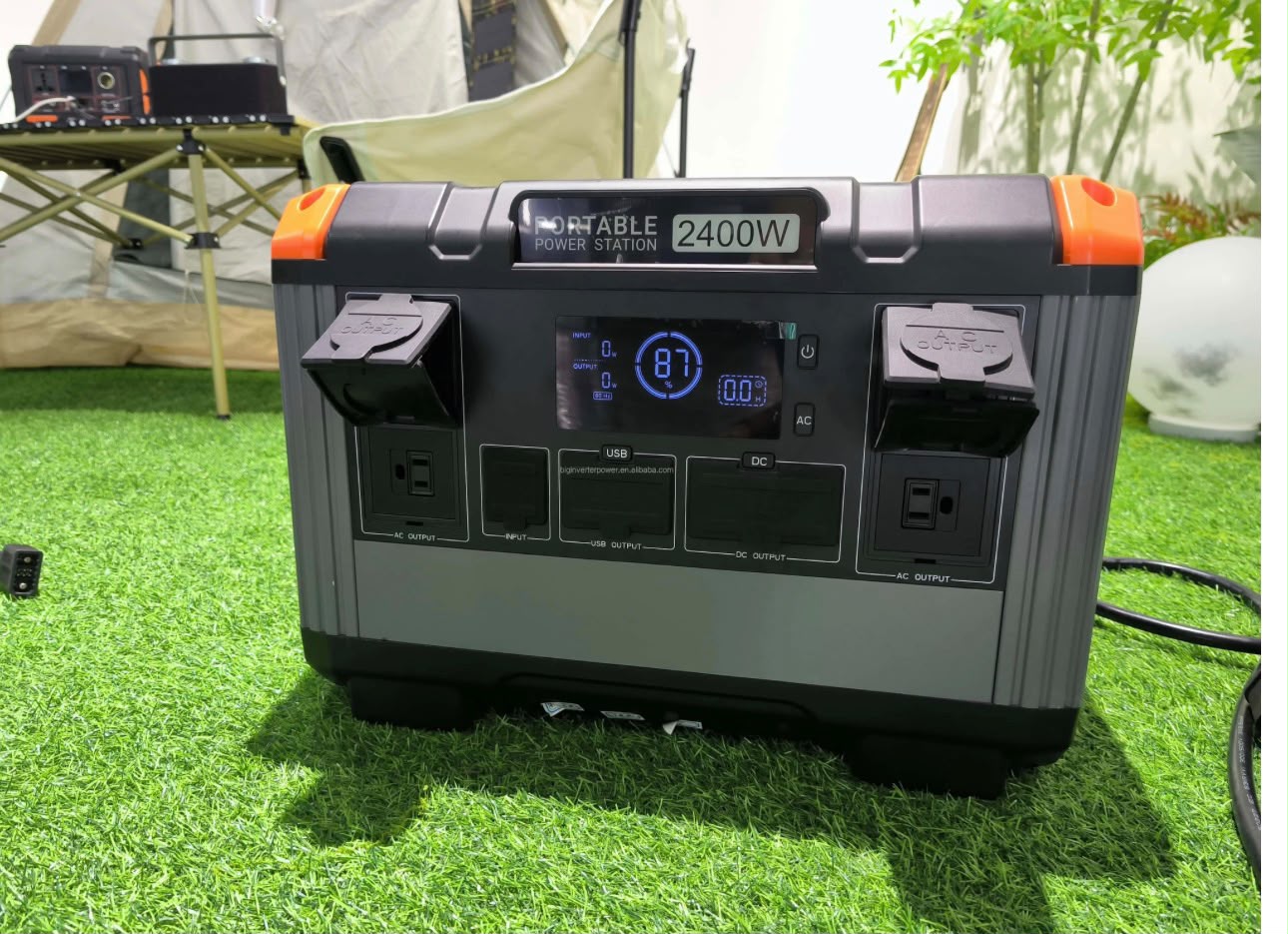 OA PowerCore 2400 portable power station set up outdoors beside a camping tent, display showing 87% charge